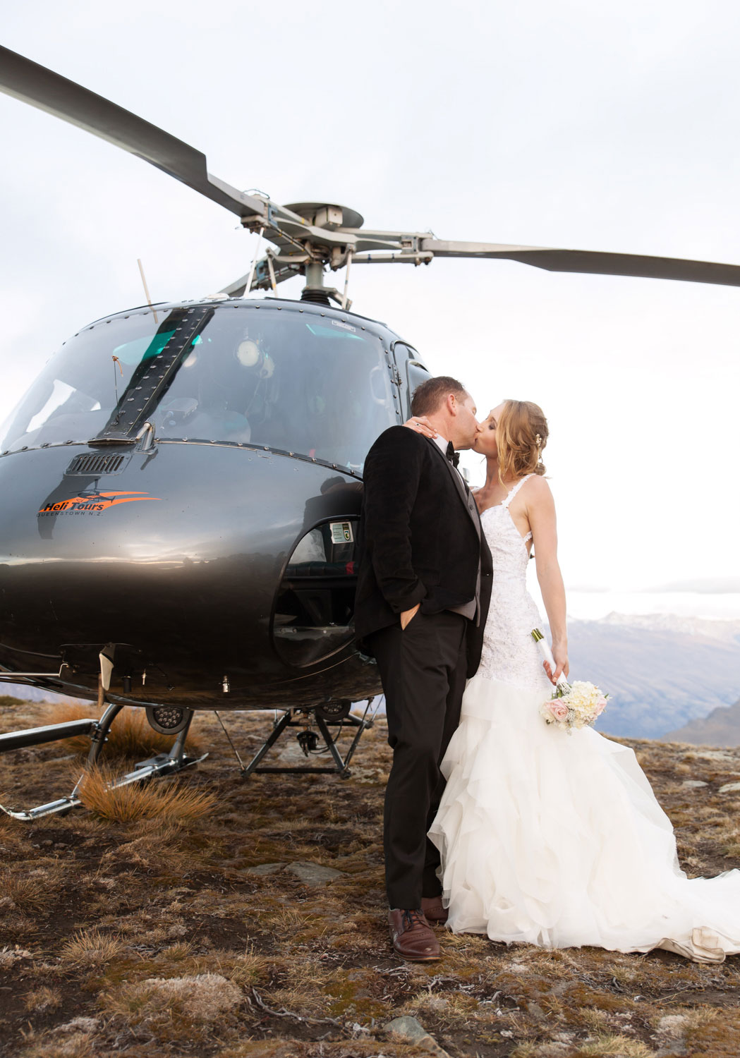 destination wedding couple kissing beside helicopter
