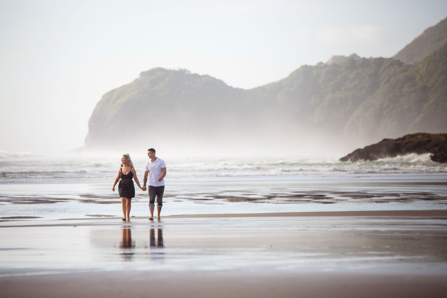 couple walking along piha beach