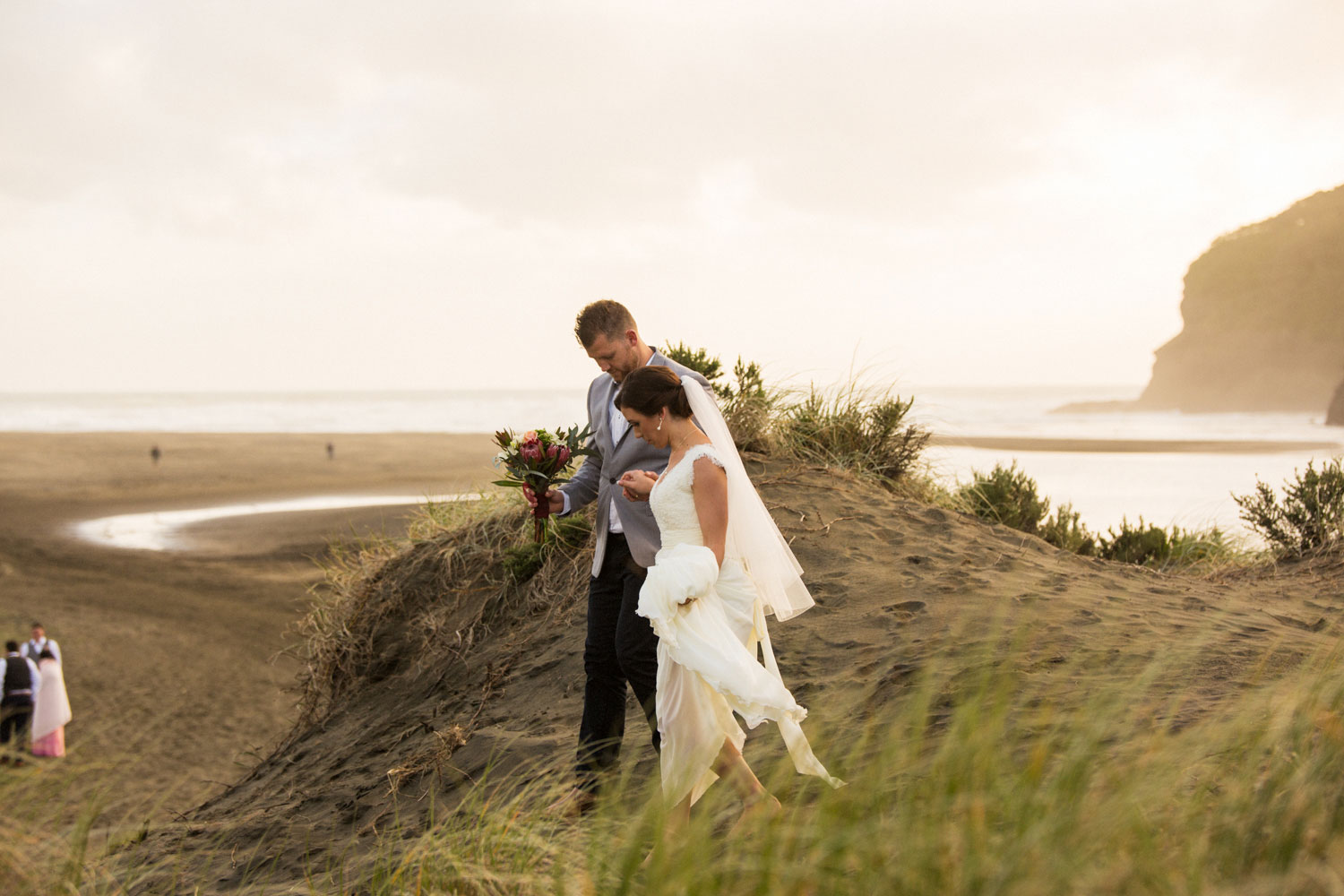 bride and groom walking on bethells beach