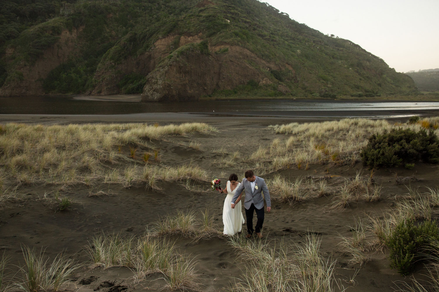bride and groom walking on bethells beach dunes