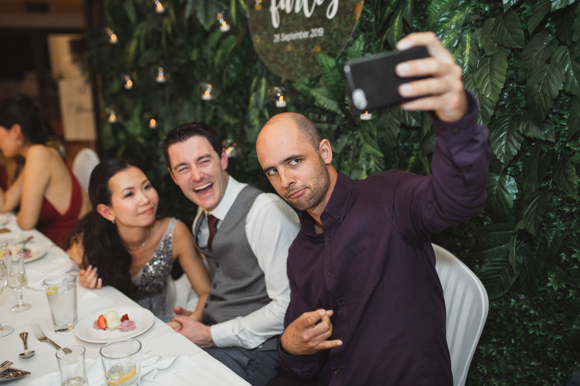 guest taking a selfie with bride and groom