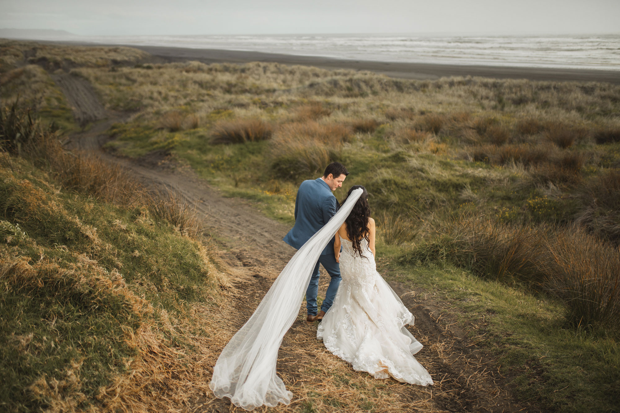 bride and groom walking on karioitahi beach